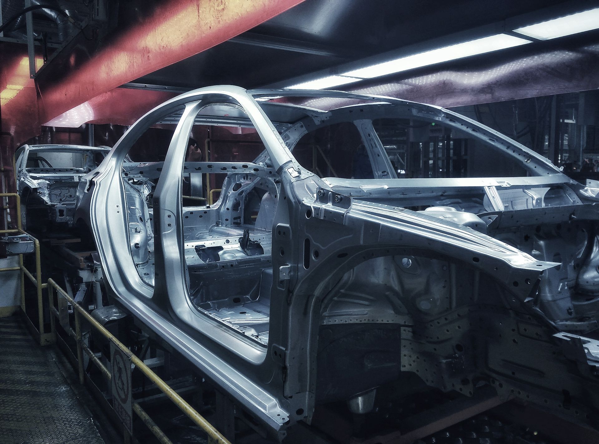 Bare car body shells on an assembly line in an auto factory with red overhead lighting