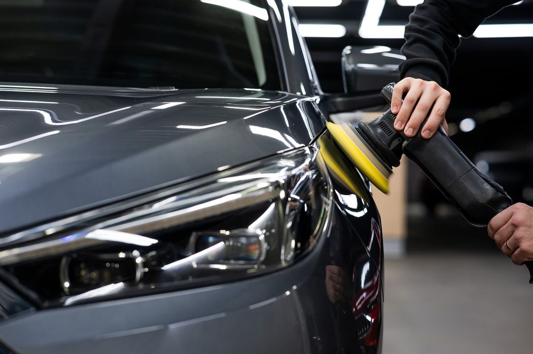 Hand polishing a dark gray car with a yellow buffer in a garage