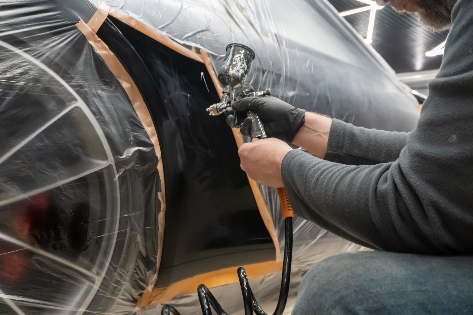 Worker spray-painting a black car panel in an automotive repair shop