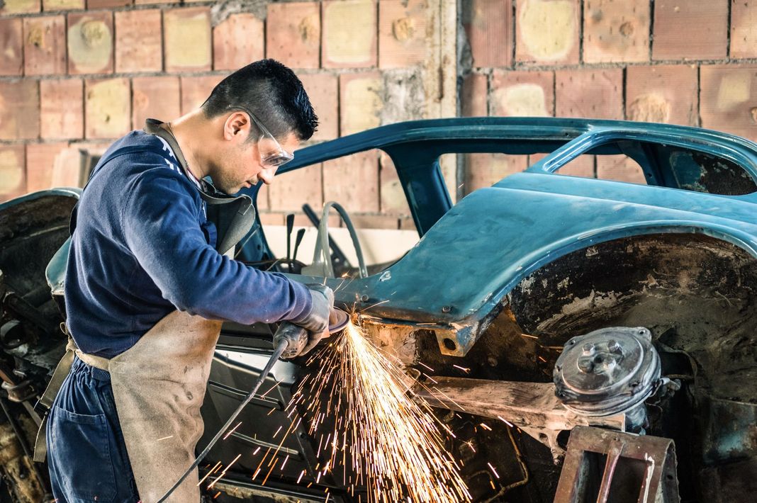 Mechanic grinding metal on a blue car body in a workshop, sparks flying.