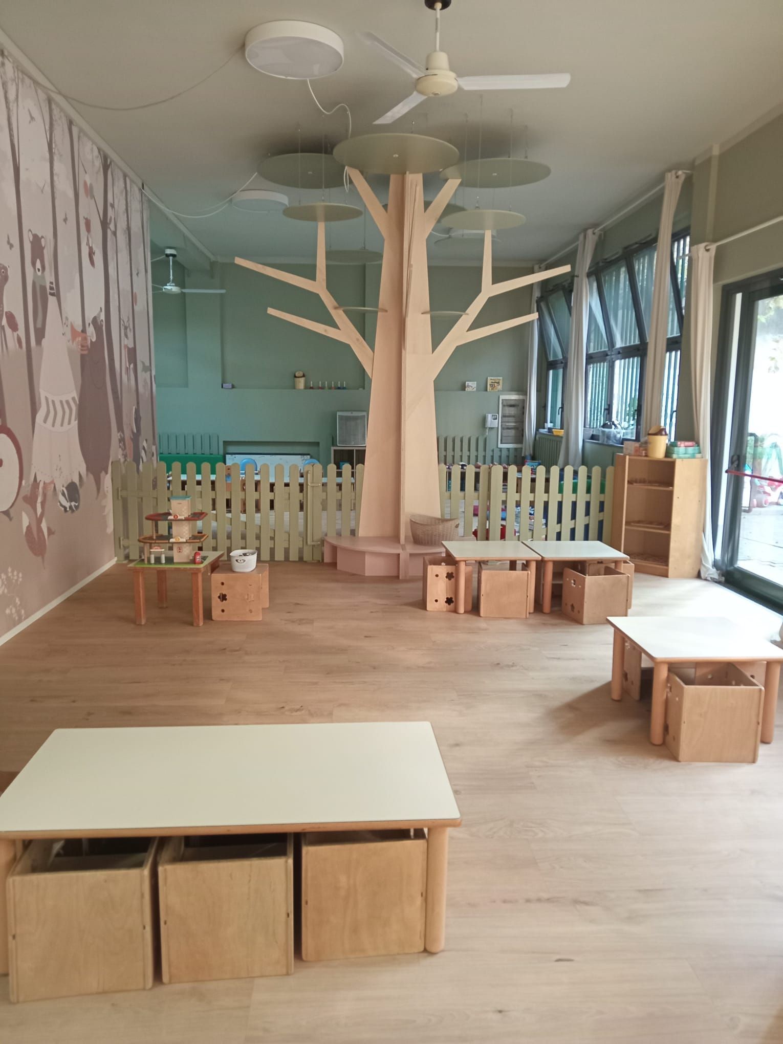 Un'aula luminosa e ariosa, con mobili in legno, un albero intagliato e dischi decorativi appesi.