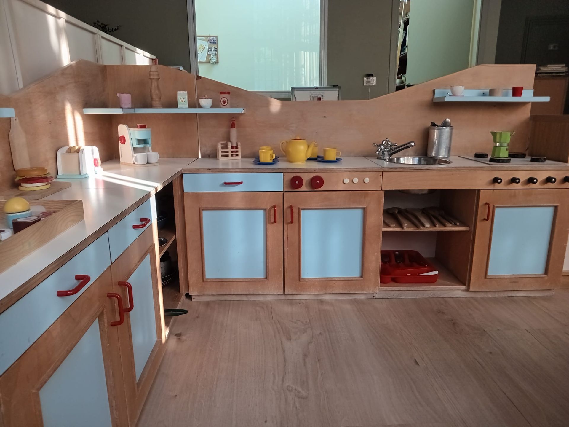 Cucina giocattolo con mobili in legno, dettagli blu, elettrodomestici giocattolo e un piano di lavoro in legno.