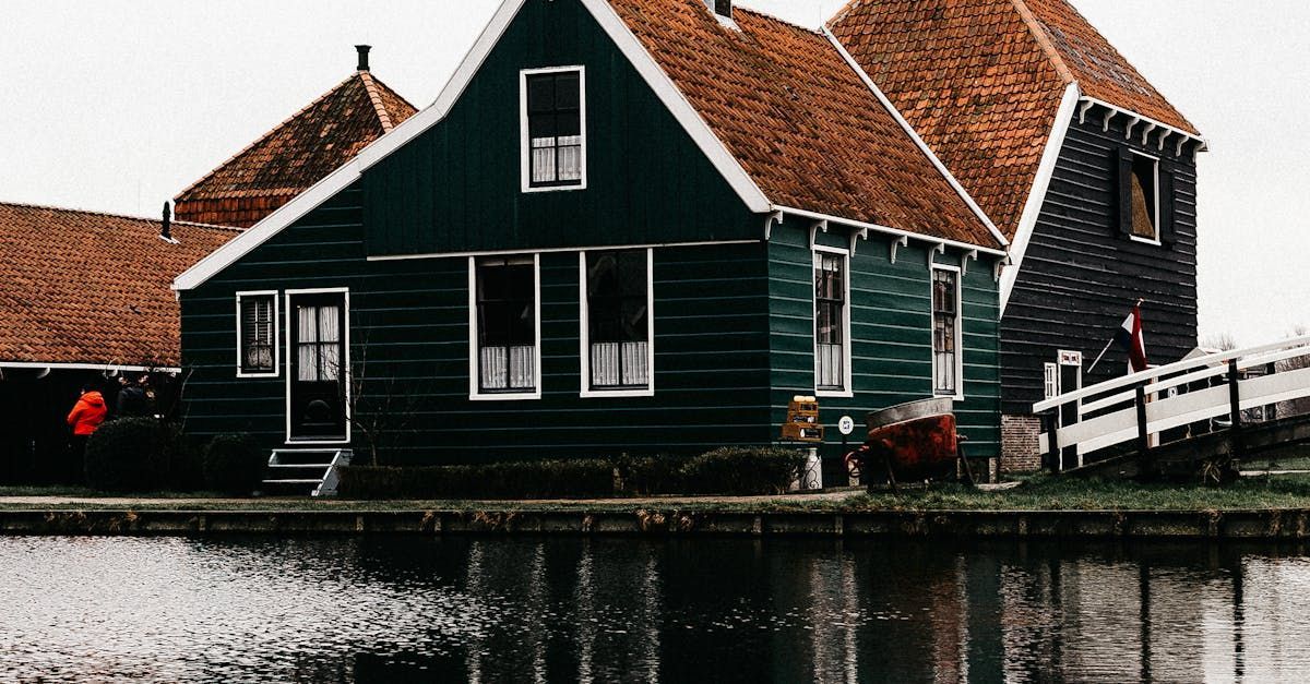 A green house with a red roof is next to a body of water.