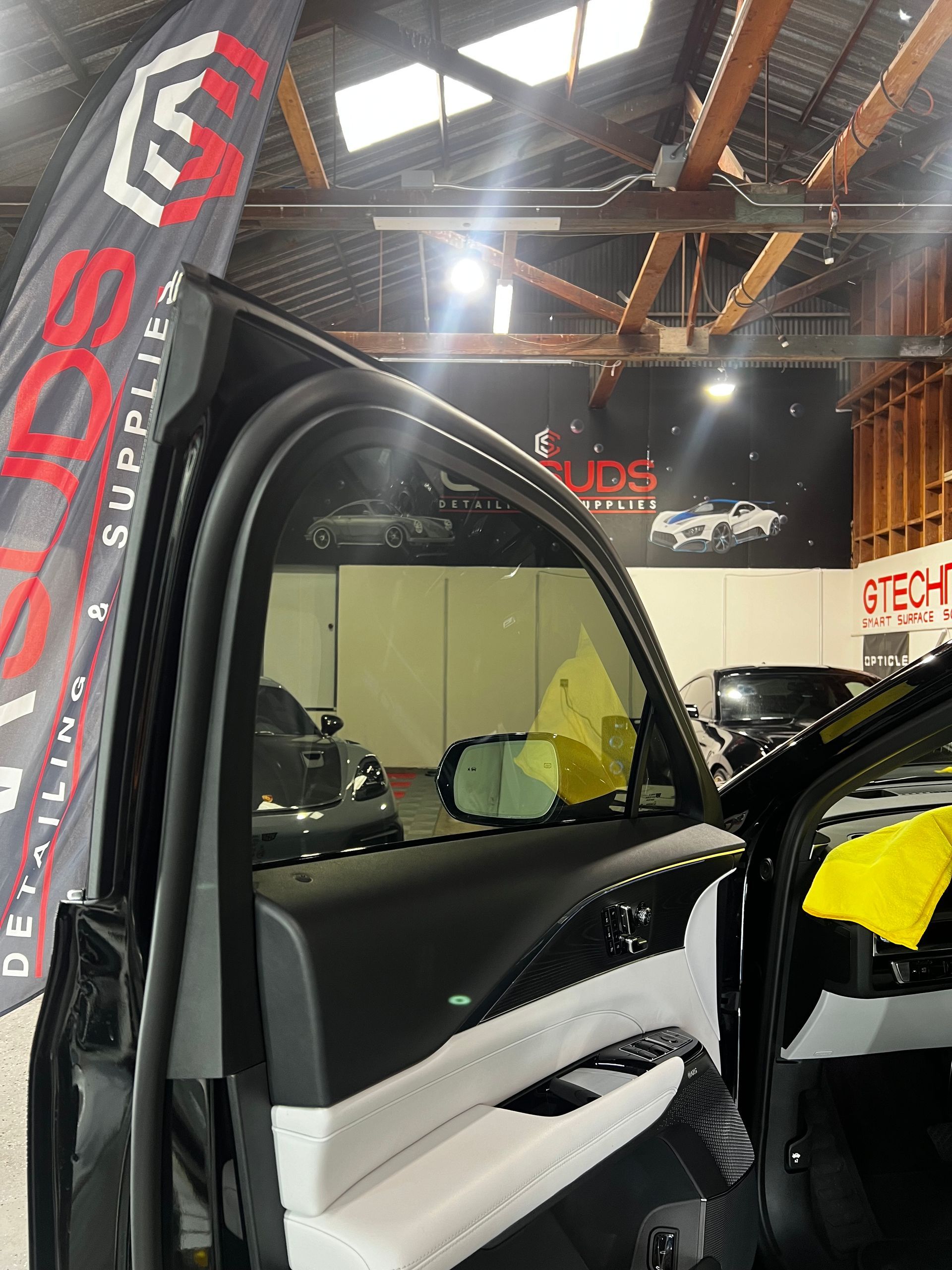 A black car is being cleaned in a garage with a flag hanging from the roof