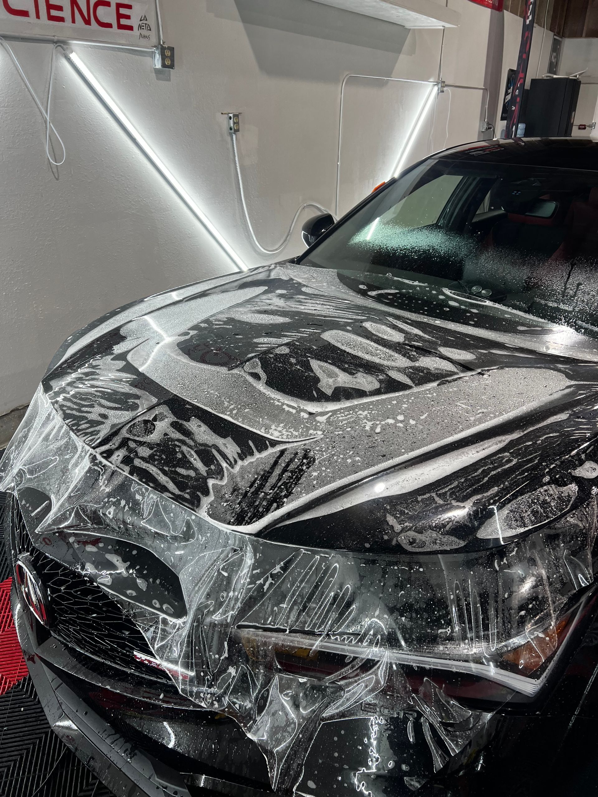 A black car is covered in plastic wrap in a car wash.