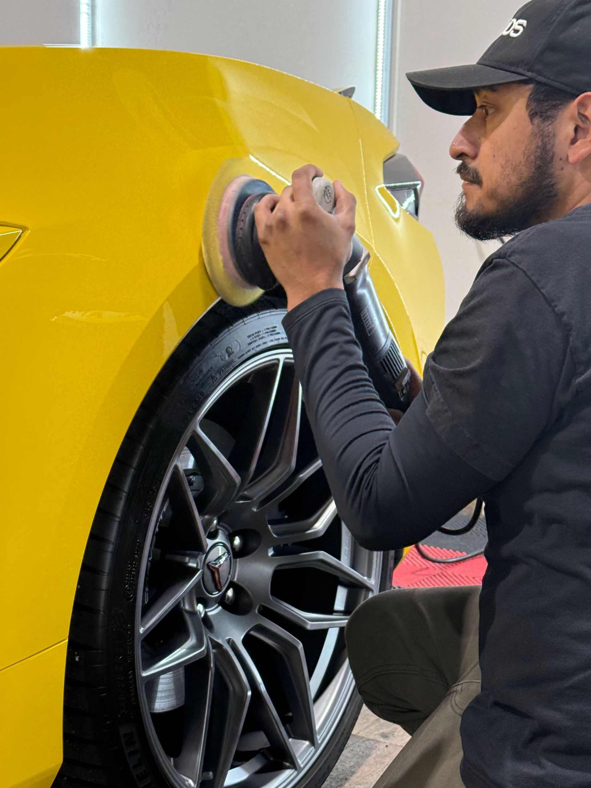 A man is polishing a yellow car with a polisher