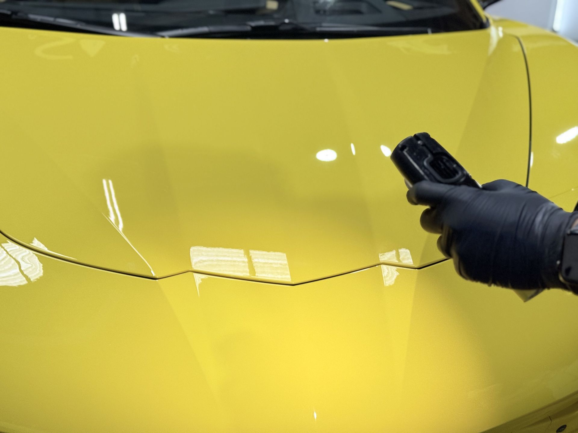 A person is holding a remote control in front of a yellow car.