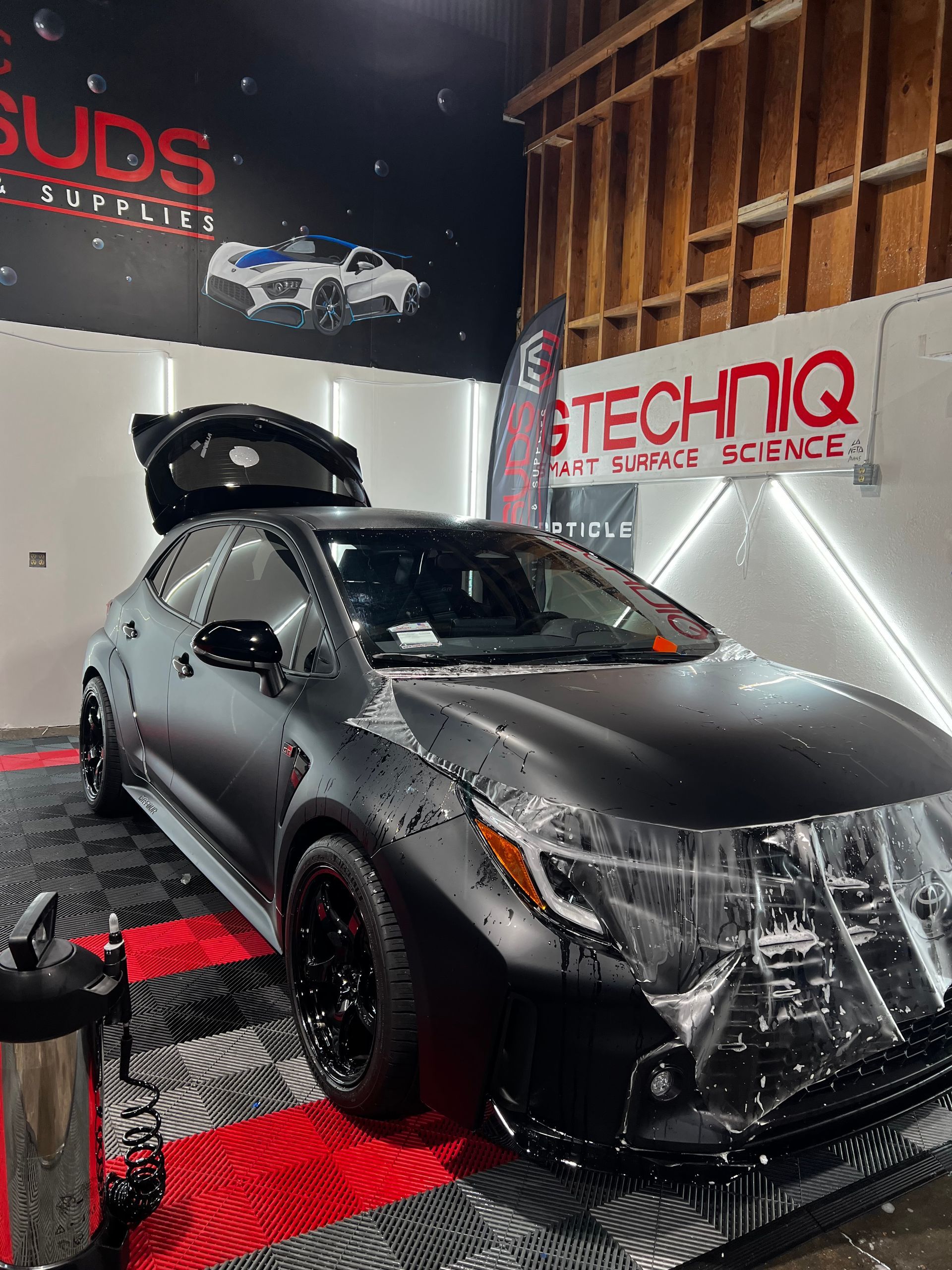 A black car is parked in a garage with the hood up.