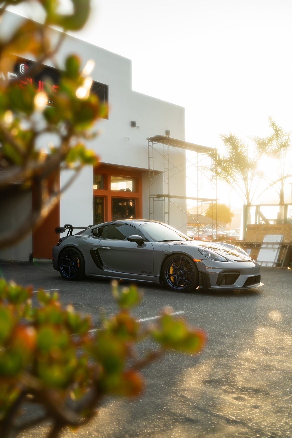 A gray sports car is parked in a parking lot in front of a building.