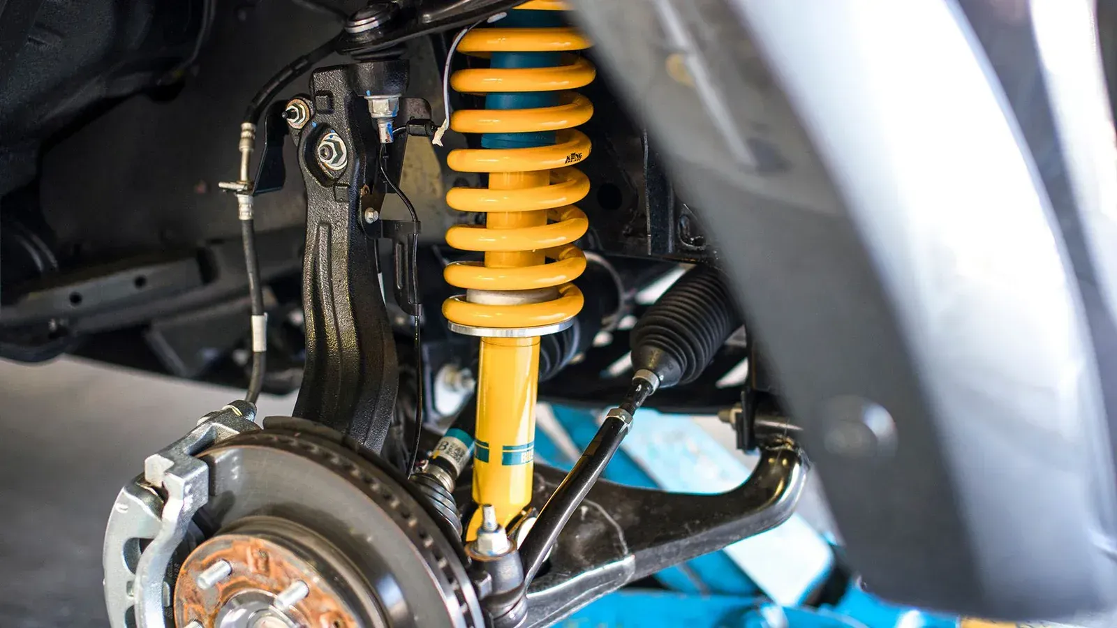 Yellow shock absorber and spring assembly on a car's suspension system — Chris Albertini Automotive in North Lismore, NSW