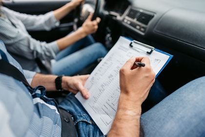A man is sitting in a car writing on a clipboard.
