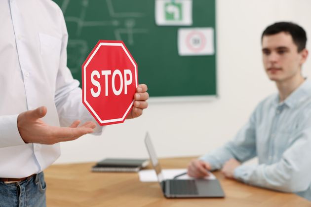 A man is holding a stop sign in front of a man sitting at a table.