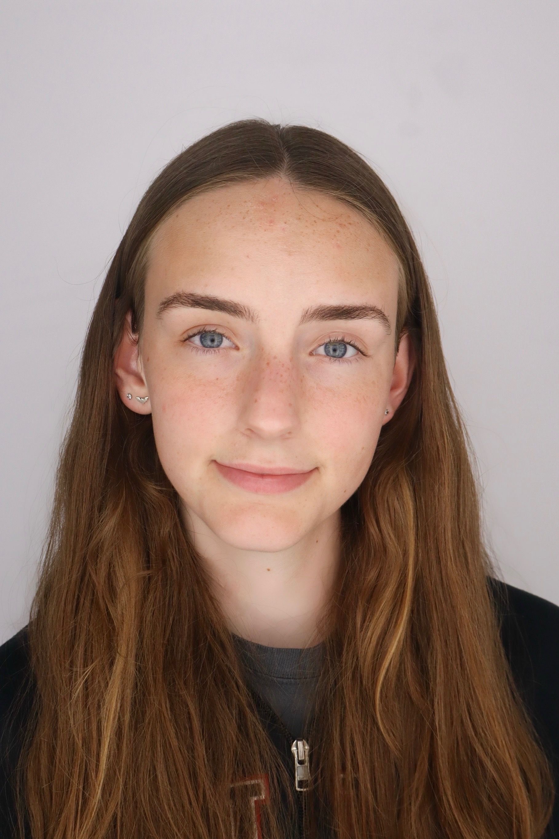 Portrait of a person with long brown hair, blue eyes, and a slight smile against a plain light background
