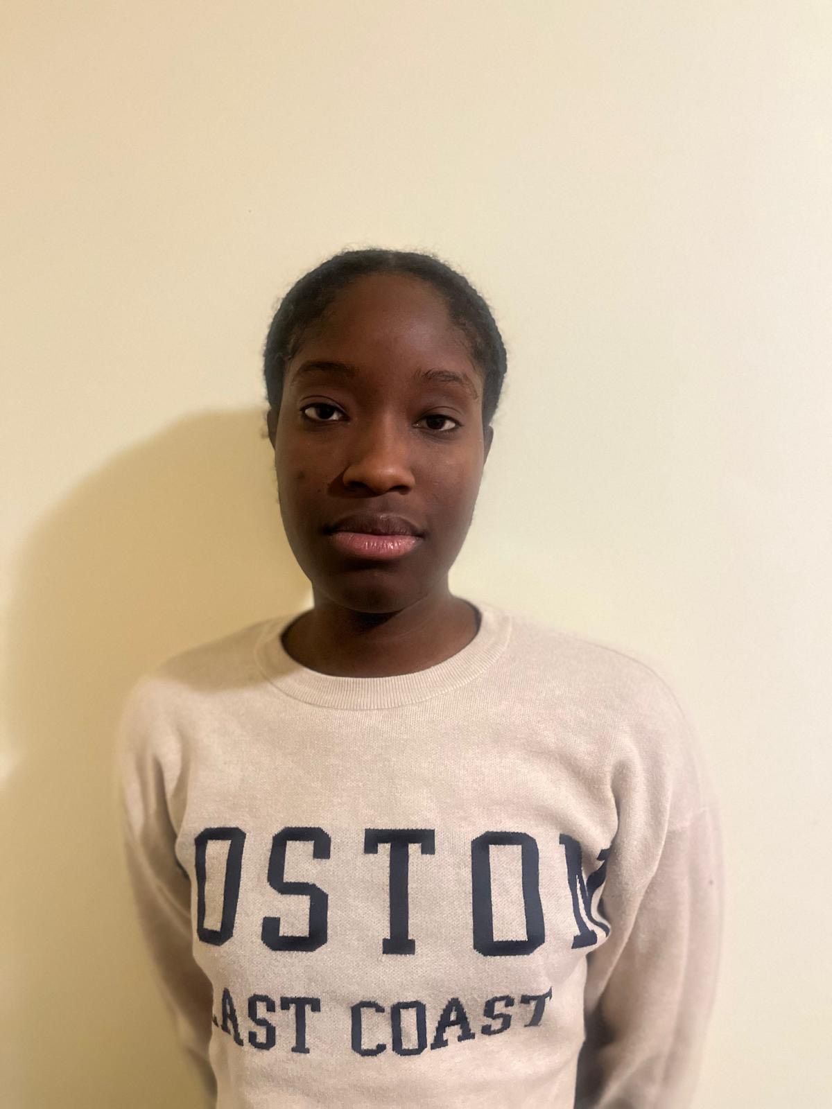 Person standing against a beige wall wearing a white Boston East Coast sweatshirt.