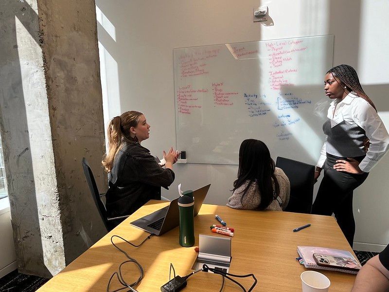 Three people discuss ideas at a whiteboard in a bright office
