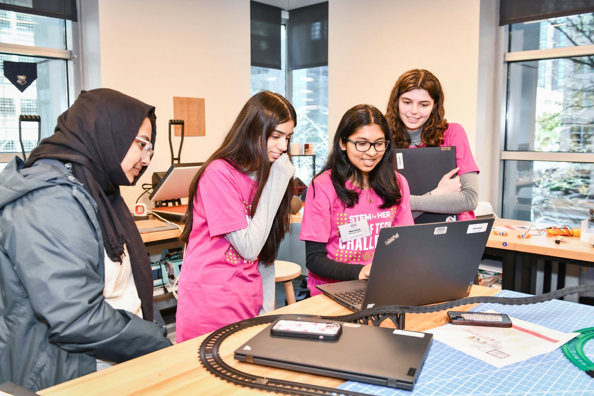 Four people gathered around a laptop in a bright office, collaborating and pointing at the screen.
