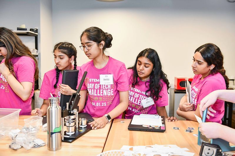 Students in pink shirts working with lab equipment at a classroom table