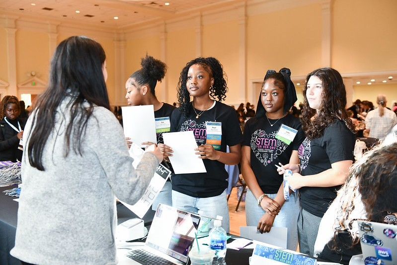 People at a networking booth exchanging brochures in a bright conference hall