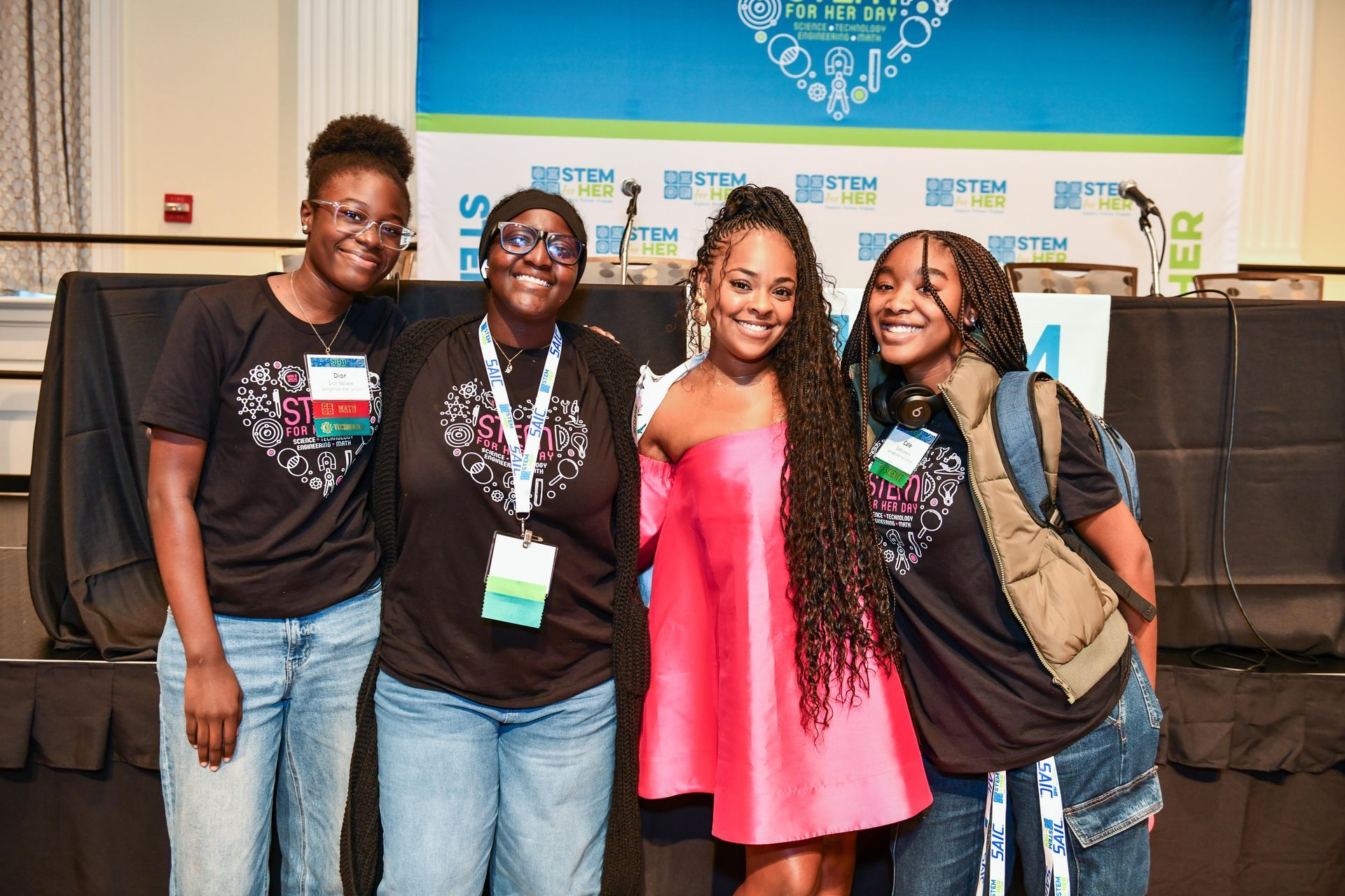 Four smiling people posing indoors with lanyards in front of a blue banner.