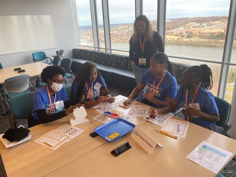 People collaborating around a table with papers and folders in a bright room with a large window.