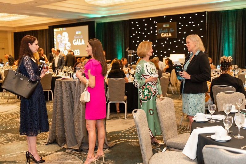 Guests chatting at a gala reception with cocktail tables and chandeliers in a decorated ballroom.