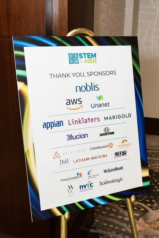 Sponsor logo poster on an easel at a conference, with various company logos on a white sign.