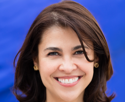 Smiling woman with shoulder-length brown hair against a blue background
