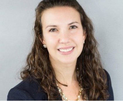 Smiling woman with curly dark hair in a navy top against a light gray background