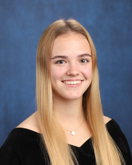 Smiling portrait against a blue studio backdrop, wearing a black top and a silver necklace.