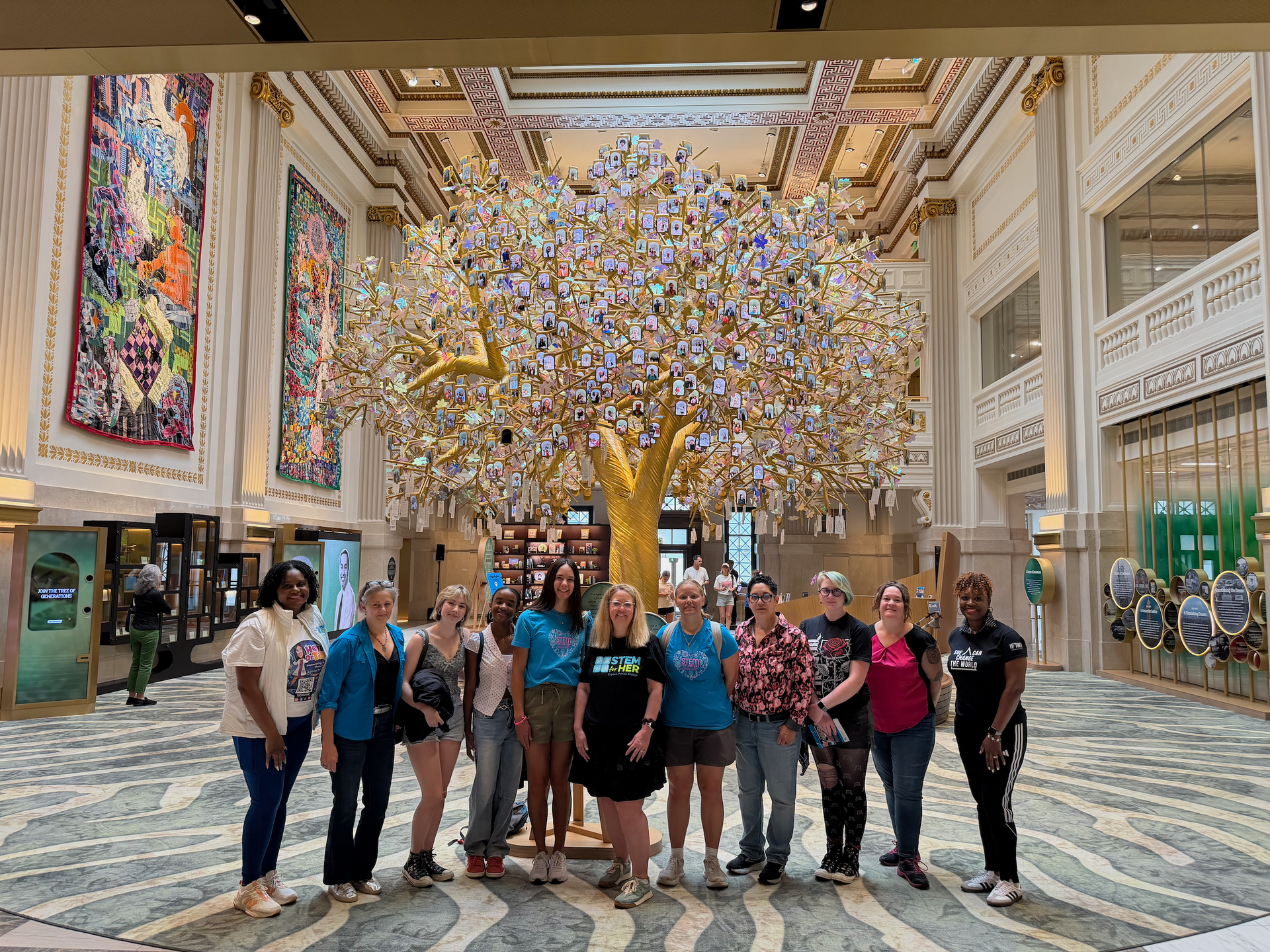 Group of people posing in a grand hall beneath a large, glowing tree sculpture