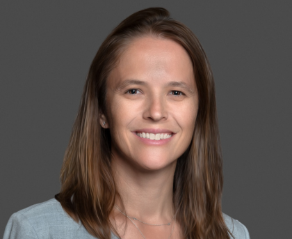Smiling woman with shoulder-length brown hair against a gray background.