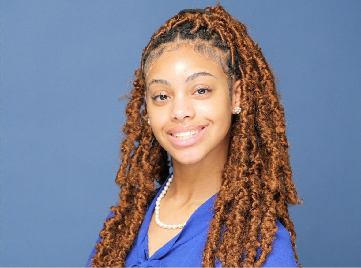Portrait of a smiling woman with long braids, wearing a blue top against a plain blue background