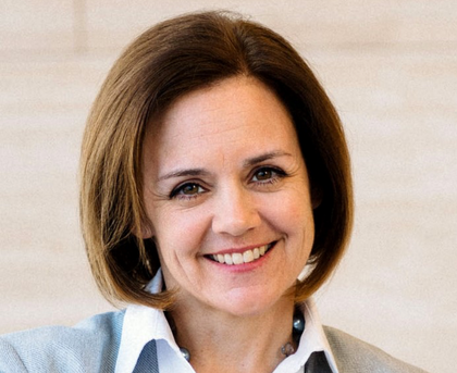 Smiling woman with short brown hair in a light-colored blazer against a soft beige background