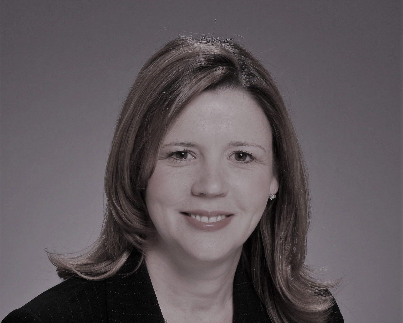 Studio portrait of a smiling woman in a dark blazer against a gray background