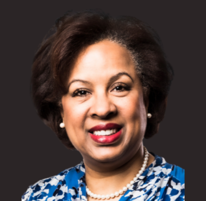 Smiling woman in blue patterned blouse and pearl necklace on a dark background