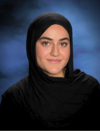 Studio portrait of a person in a black headscarf against a blue backdrop, smiling slightly.