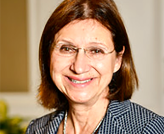Smiling woman with glasses in a striped blouse, standing indoors against a blurred background