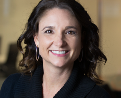 Smiling woman in a dark sweater, with shoulder-length dark hair, against a softly blurred indoor background