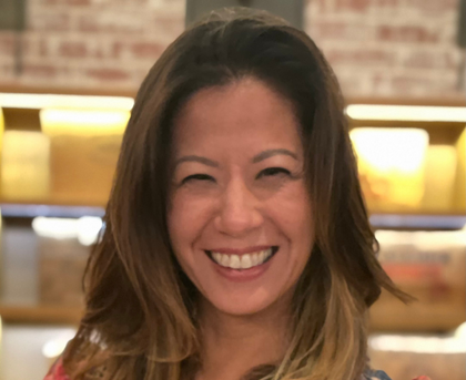 Smiling person in a warmly lit indoor setting with blurred shelves in the background