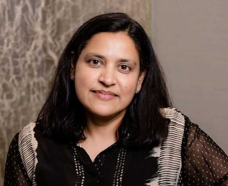 Portrait of a smiling woman with shoulder-length dark hair against a neutral patterned background