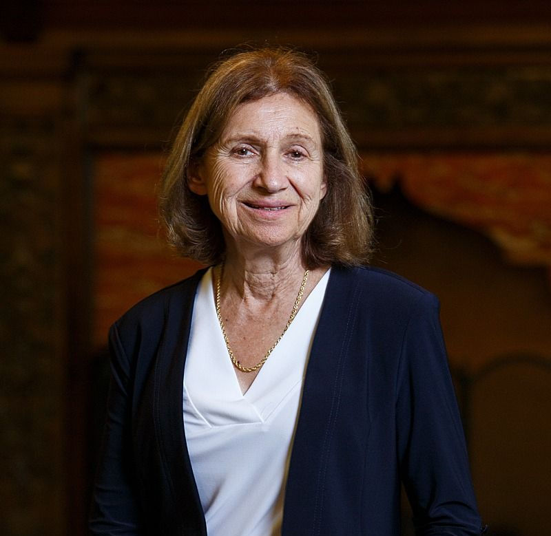 Portrait of a smiling woman in a navy blazer and white top against a dark background