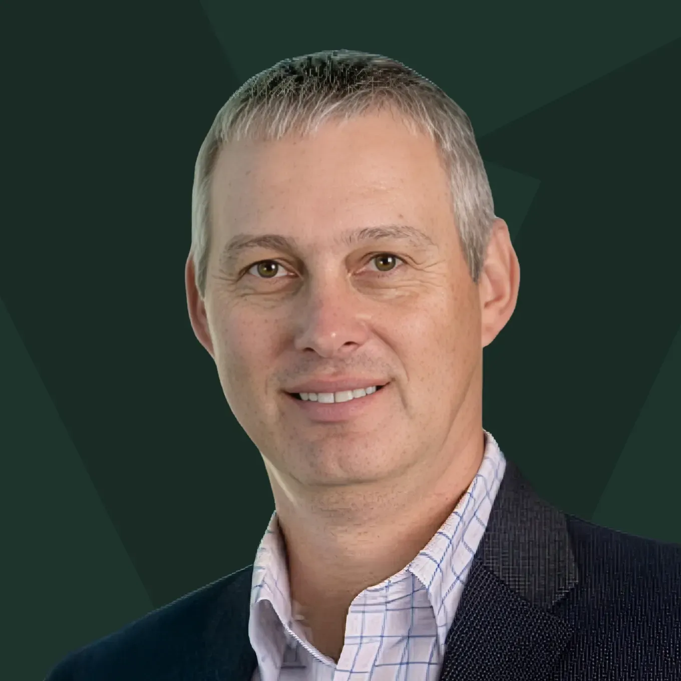 Portrait of a smiling man in a blazer and collared shirt against a dark green background