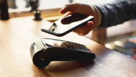 Person holding a smartphone over a card payment terminal on a wooden table