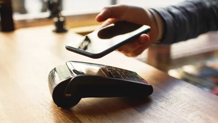Person holding a smartphone over a card payment terminal on a wooden table