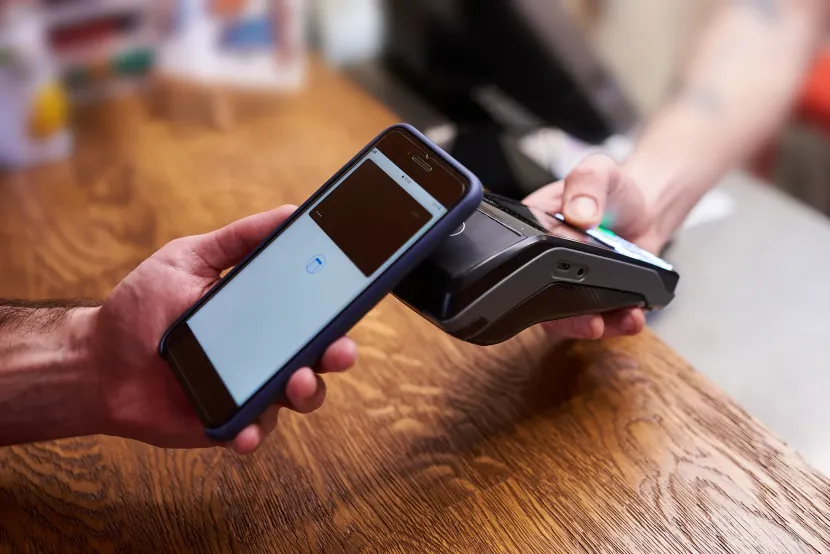 Person using a smartphone to tap a payment terminal on a wooden table