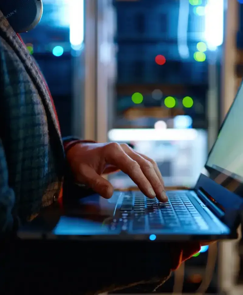 Hands typing on a laptop with blurred server lights in the background