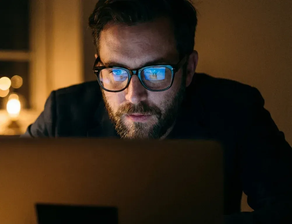 Man in glasses working on a laptop in dim warm light