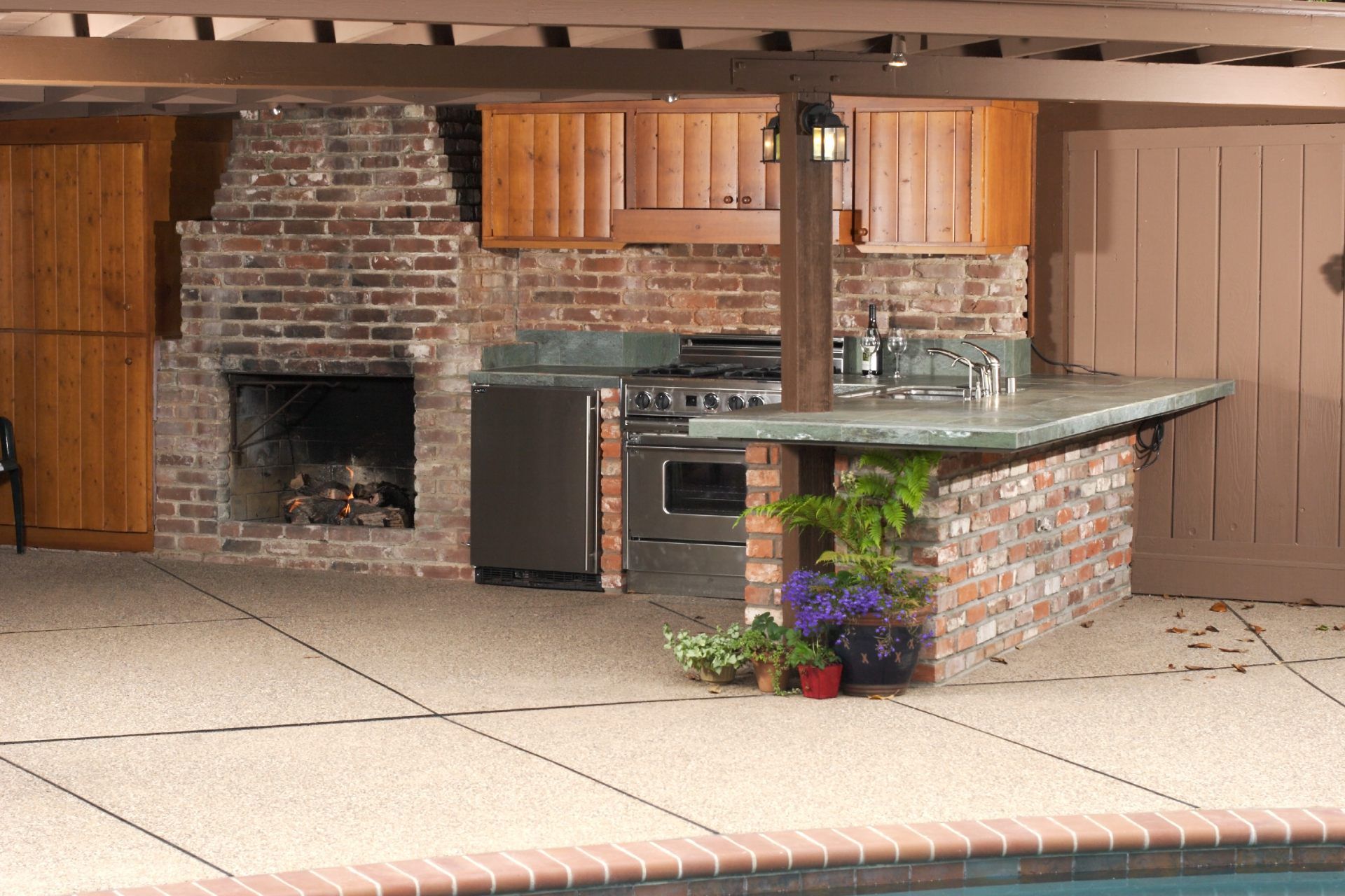 Outdoor kitchen with brick construction, fireplace, and built-in grill near a pool.