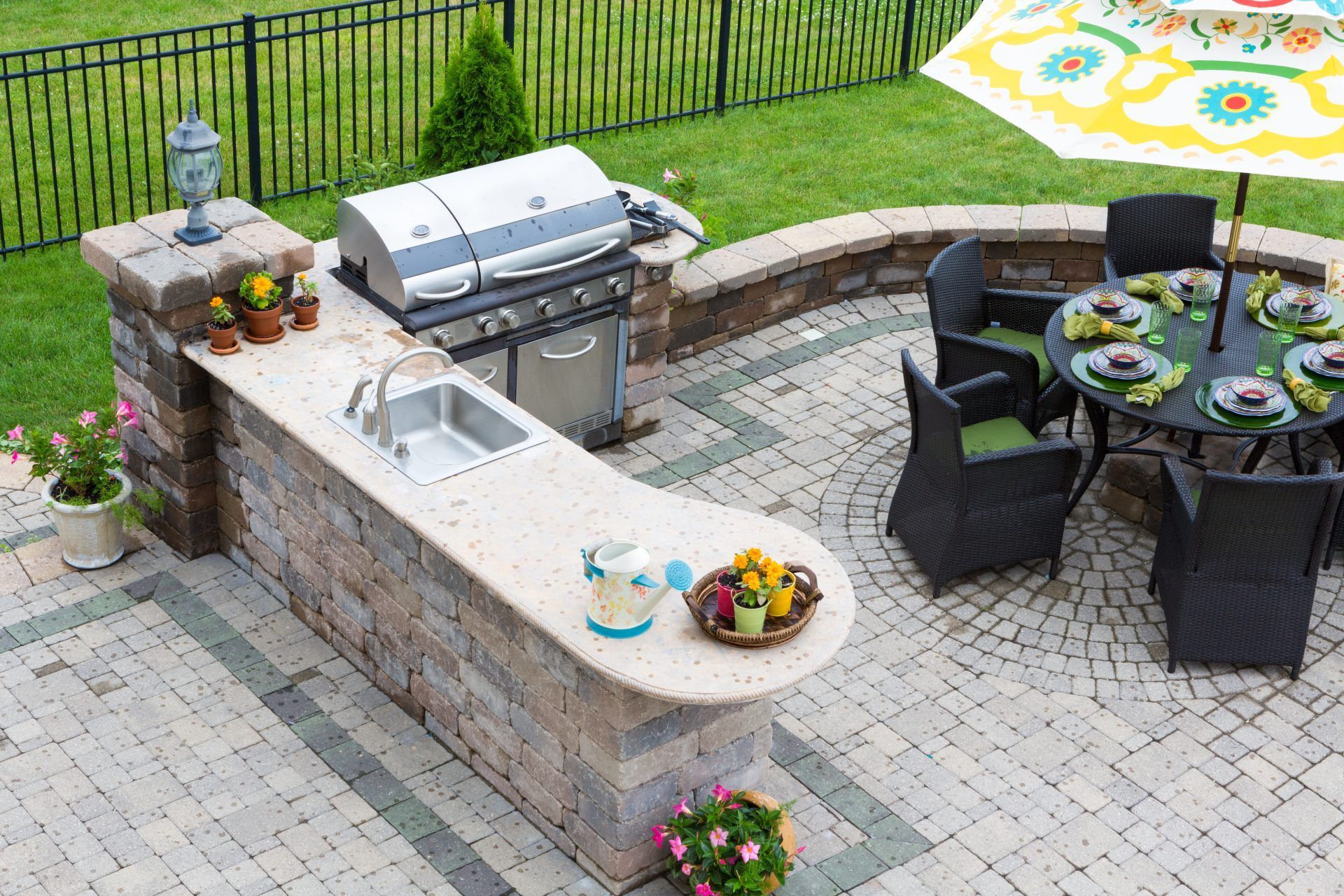 Outdoor kitchen with grill, sink, and seating area under an umbrella on a patio.