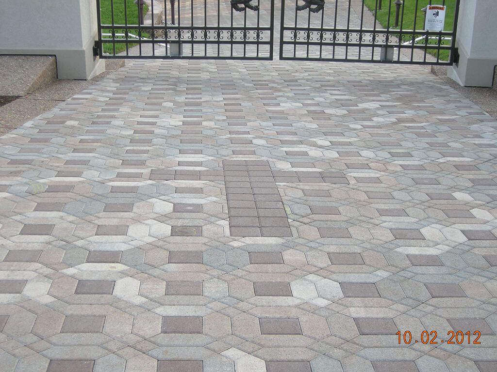 Paver driveway with geometric pattern leading to a black wrought iron gate.